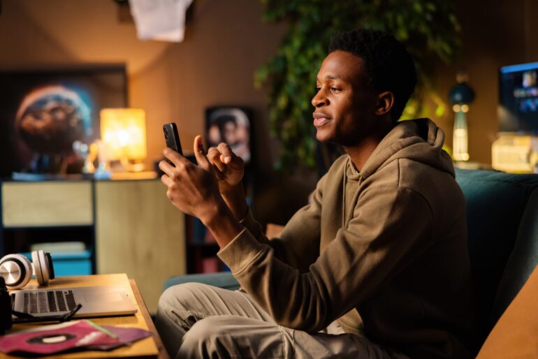 African American man could be a documentary filmmaker, using his phone to record interviews and location scouting while editing footage on his laptop