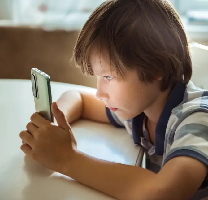 Young boy sitting at a table intently looking at a smartphone.